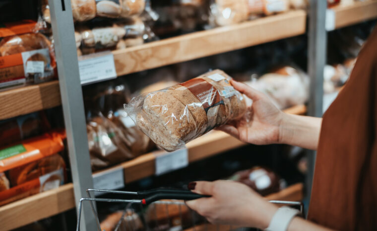 hand håller upp bröd i påse i butik, i bakgrunden en brödhylla