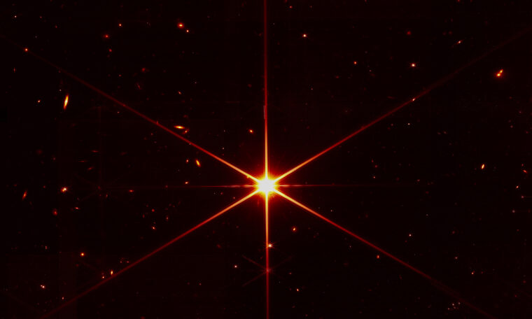 Stark ljuspunkt med gulröda strålar i centrum av den svarta bilden. Små ljuspunkter i marginalen