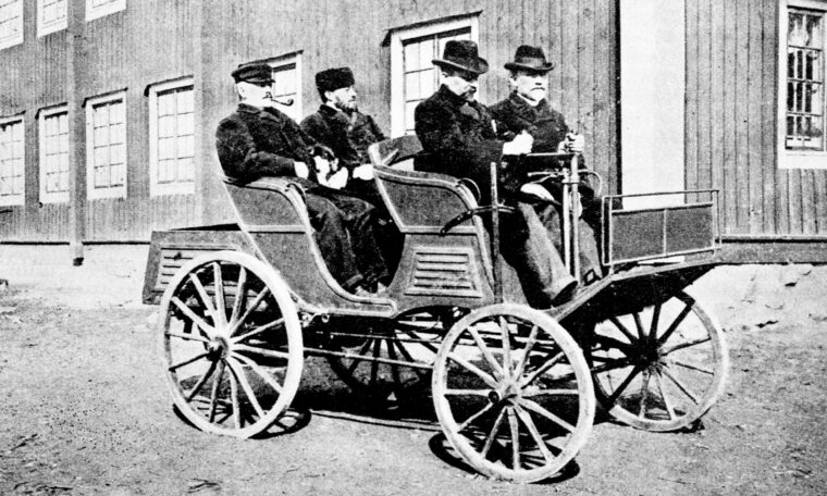 svartvitt foto av bil byggd av en hästvagn, fyra män med hattar ombord