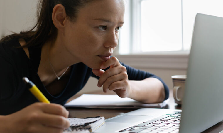 ung kvinna framåtlutad framför datorn och penna i handen