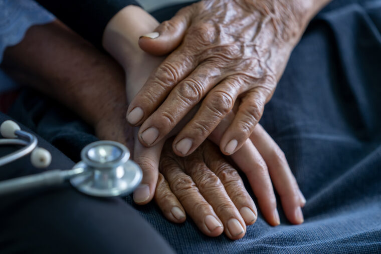 Två händer som tillhör en äldre person håller en yngre persons hand.