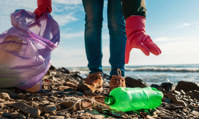 En plastflaska plockas upp från stranden för att lägga i påse