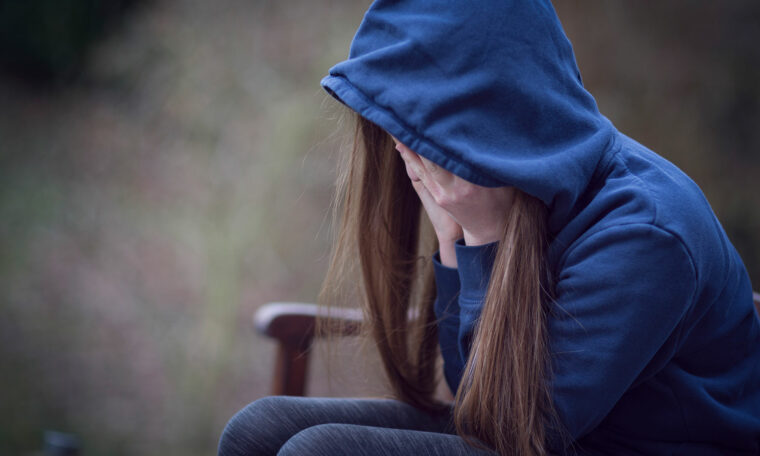 ung flicka sitter på en bänk utomhus med ansiktet i händerna