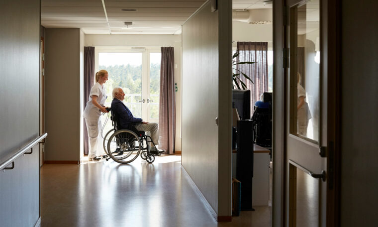 man i rullstol som körs av kvinna i vita arbetskläder