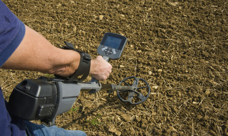 En man riktar en metallsökare mot marken på en plöjd åker.