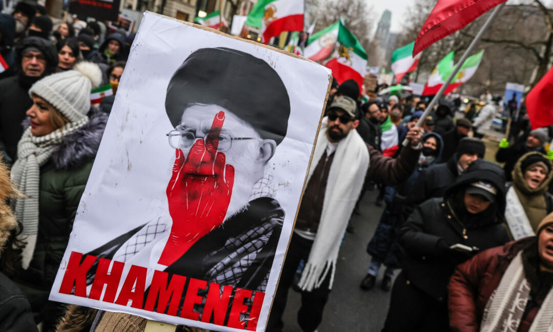 Demonstranter håller upp bild på ayatolla Khamenei med en hand som pekar finger målad över hans ansikte.