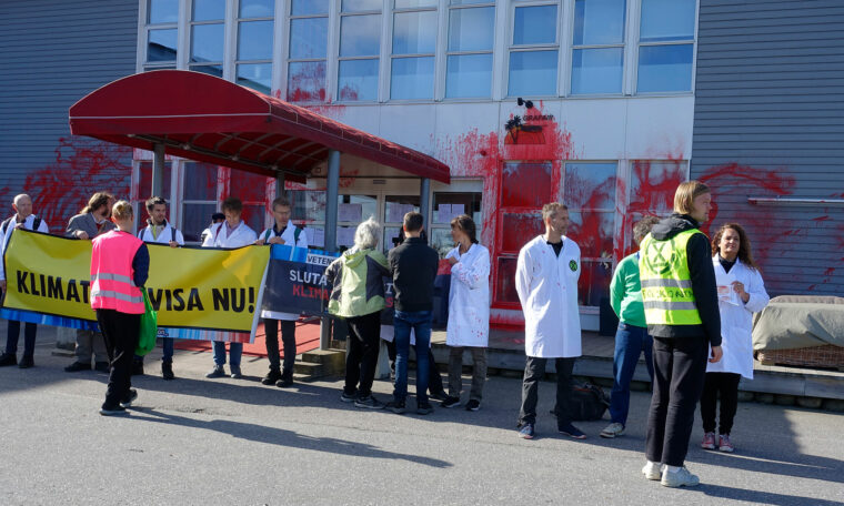 demonstranter med skultar om klimatet har hällt något som ska likna blod på en byggnad, flera har labbrockar på sig