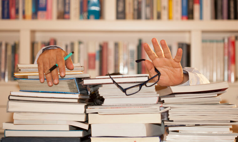 två händer viftar bakom högar med rapporter och papper